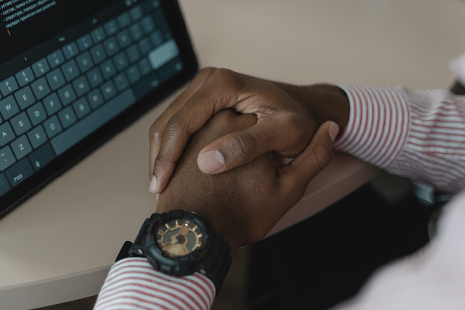 Close-up image of crossed hands wearing a watch near a tablet keyboard.